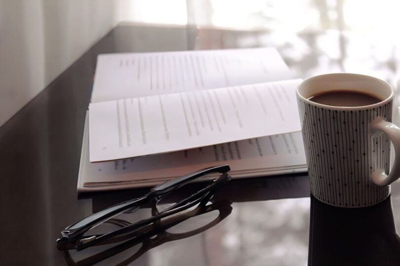 机の上に開いた本とコーヒー、眼鏡